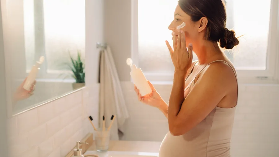 Mujer embarazada aplicándose crema facial frente al espejo